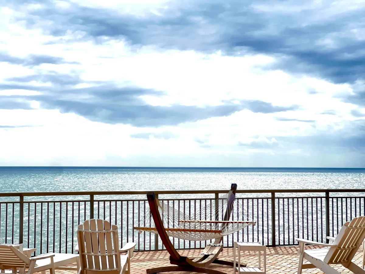 This exterior scene shows a tranquil beachfront setup with a hammock and beach chairs overlooking the ocean. The setting feels private and serene, with the gentle waves and an inviting sandy stretch creating a perfect backdrop for romantic relaxation. The mood is peaceful, ideal for quiet mornings or starlit evenings.