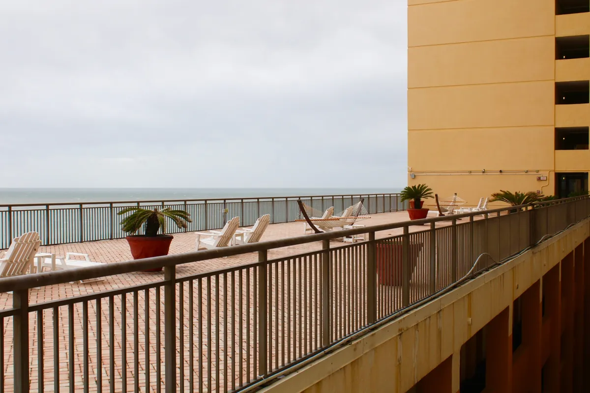 A private balcony with lounge chairs and potted plants, framed by a balcony railing, opens up to a stunning panoramic ocean view. The inviting seating encourages relaxation, reading, or conversation while soaking up the sea breeze and natural beauty.