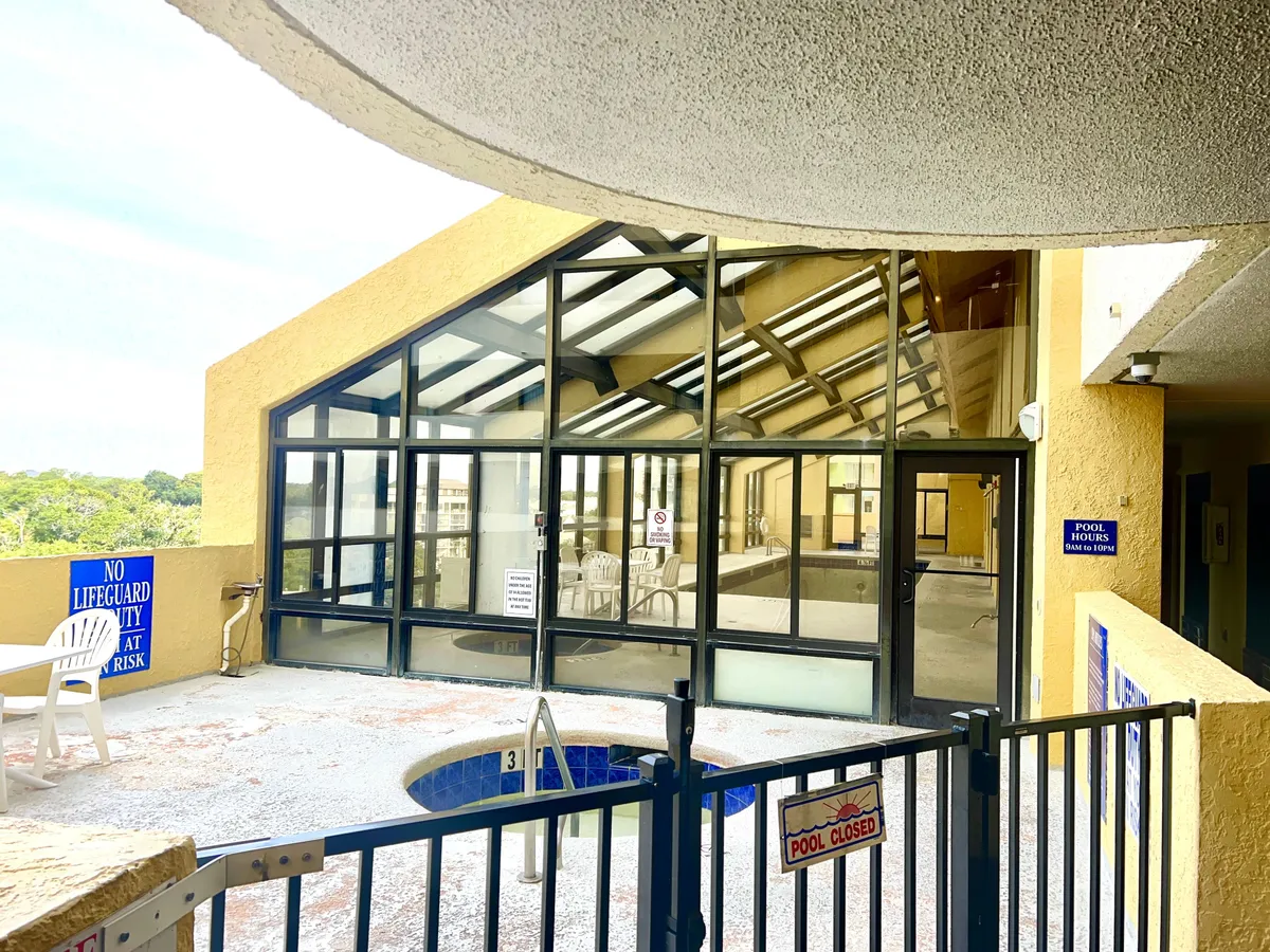 An inviting indoor pool area with a hot tub, glass walls letting in natural light, lounge chairs, and poolside seating. The ambiance is tranquil and spa-like, ideal for relaxation and unwinding after a day of activities.
