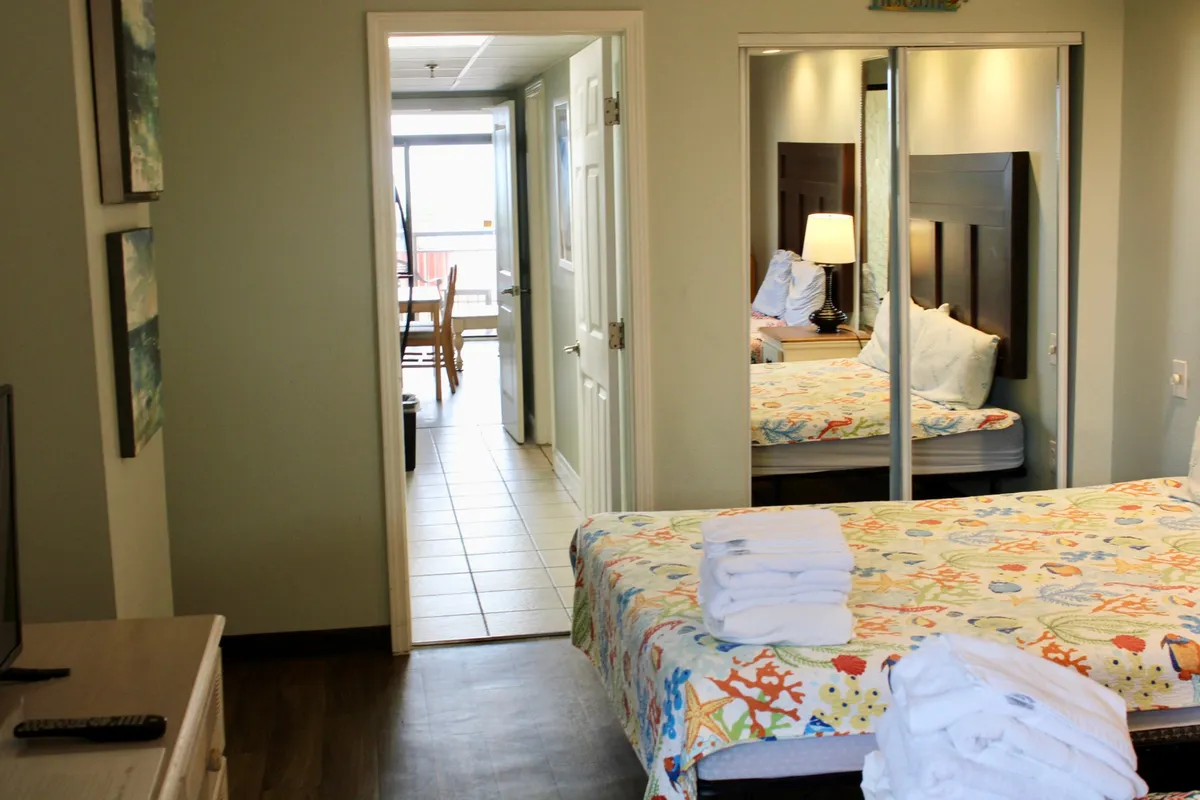 A cheerful bedroom scene with a colorful bedspread adorned with marine life patterns, a mirrored wardrobe, and a view into the outdoor space. The room is bright and airy, filled with natural light, emphasizing a fresh start to the day.
