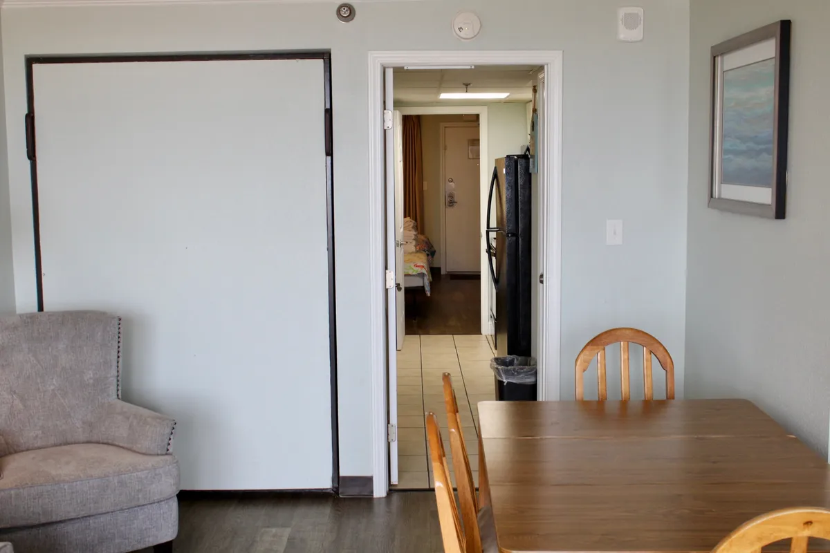 A cozy dining area is shown, featuring a dining table with surrounding chairs and an armchair nearby. The open doorway hints at a seamless flow between the kitchen and living spaces, suggesting a place where guests can enjoy meals together, relax, or gather for family conversations.
