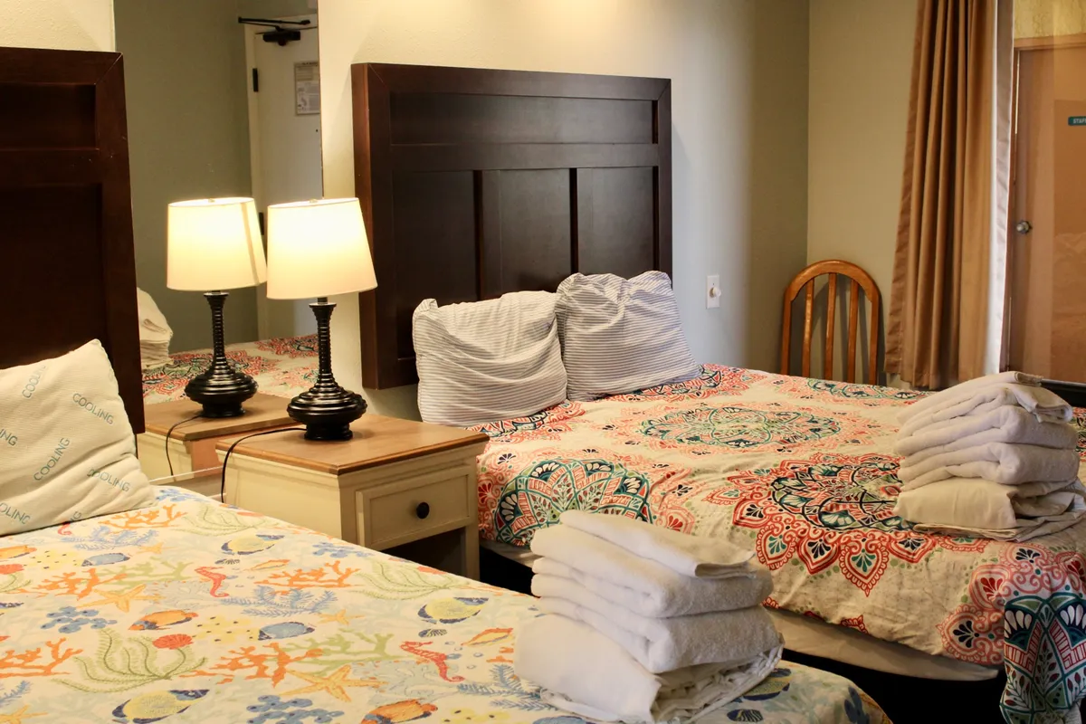 A cozy bedroom featuring a bed dressed in a colorful quilt, with decorative pillows and soft lighting from bedside lamps. The setting emphasizes comfort and warmth, with tranquil decor and an inviting ambiance.